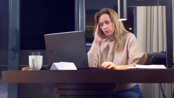 Γυναίκα που εργάζεται σε ένα φορητό υπολογιστή σε ένα τραπέζι τη νύχτα σε ένα δωμάτιο ξενοδοχείου. 4 k. αποκοιμιέται στον εργασιακό χώρο, χασμουρητά. — Αρχείο Βίντεο
