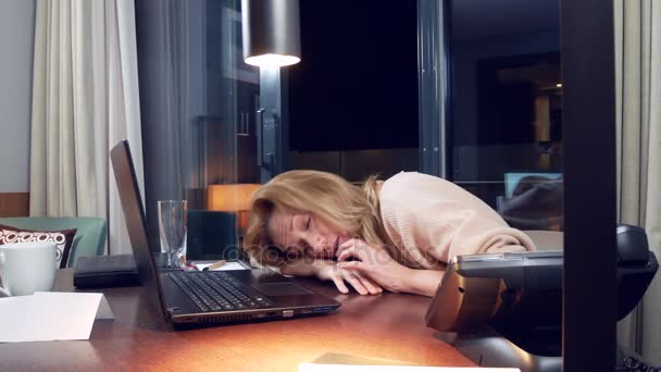 Mujer trabajando en un portátil en una mesa por la noche en una habitación de hotel. 4k. se queda dormida en el lugar de trabajo, una llamada la despierta  .. — Vídeos de Stock