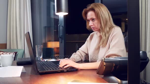 Γυναίκα που εργάζεται σε ένα φορητό υπολογιστή σε ένα τραπέζι τη νύχτα σε ένα δωμάτιο ξενοδοχείου. 4 k. αποκοιμιέται στον εργασιακό χώρο, χασμουρητά. — Αρχείο Βίντεο