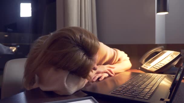 Mujer trabajando en un portátil en una mesa por la noche en una habitación de hotel. 4k. se queda dormida en el lugar de trabajo, una llamada la despierta  .. — Vídeos de Stock