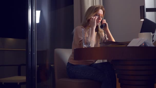 Donna che lavora su un computer portatile a un tavolo di notte in una stanza d'albergo. 4k. si addormenta sul posto di lavoro, una telefonata la sveglia  .. — Video Stock