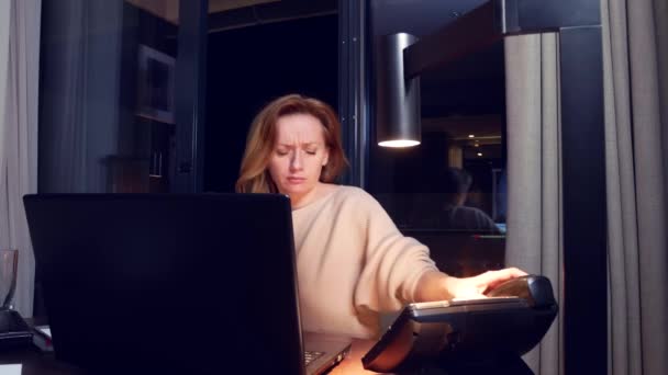 Femme travaillant sur un ordinateur portable à une table la nuit dans une chambre d'hôtel. 4k. elle s'endort sur le lieu de travail, un coup de fil la réveille  .. — Video