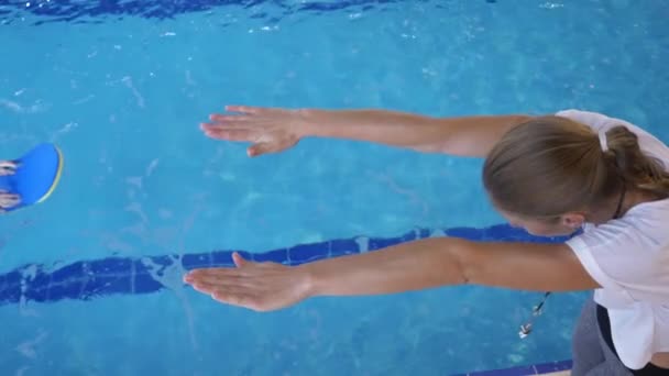 Entrenamiento de atleta de natación. El entrenador le enseña al niño a sumergirse en la piscina deportiva. 4k, cámara lenta — Vídeo de stock
