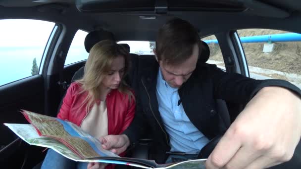 Пара чоловік і жінка подорожують в машині вздовж узбережжя, вивчаючи карту. 4k — стокове відео