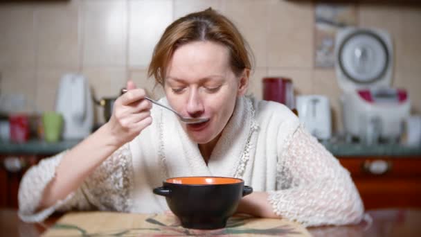 Une femme pâle en robe de chambre mange à table. Elle est fatiguée. 4k, fond flou. gros plan — Video