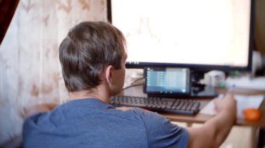 Evde mutfak masasına oturan, Döviz Alım Satım grafikteki değişiklikleri izlemek, bilgisayar monitörü arayan bir adam. arka plan bulanıklık, 4 k, freelancing