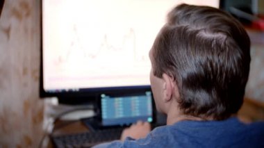 Evde mutfak masasına oturan, Döviz Alım Satım grafikteki değişiklikleri izlemek, bilgisayar monitörü arayan bir adam. arka plan bulanıklık, 4 k, freelancing