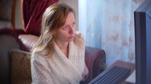Eine Frau im Bademantel und mit nassen Haaren, die zu Hause auf der Couch sitzt, Veränderungen im Wechselkursdiagramm beobachtet, auf den Computermonitor blickt, freiberuflich arbeitet, 4k, den Hintergrund verwischt — Stockvideo