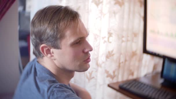 Un hombre sentado en casa en la mesa de la cocina, viendo los cambios en el gráfico de cambio de divisas, mirando el monitor de la computadora. freelancing, 4k, desenfoque de fondo — Vídeos de Stock