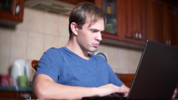 En man sitter hemma vid köksbordet, titta på förändringar i valuta exchange diagrammet, tittar på datorskärmen. frilansar, 4k, oskärpa bakgrund — Stockvideo