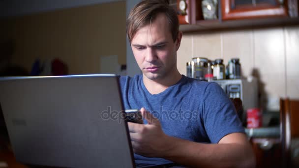 Um homem sentado em casa na mesa da cozinha, observando mudanças no gráfico de câmbio, olhando para o monitor do computador. freelancer, 4k, borrão de fundo — Vídeo de Stock