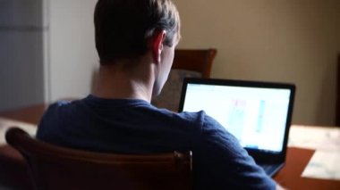 Evde mutfak masasına oturan, Döviz Alım Satım grafikteki değişiklikleri izlemek, bilgisayar monitörü arayan bir adam. arka plan bulanıklık, 4 k, freelancing