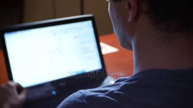 Evde mutfak masasına oturan, Döviz Alım Satım grafikteki değişiklikleri izlemek, bilgisayar monitörü arayan bir adam. arka plan bulanıklık, 4 k, freelancing