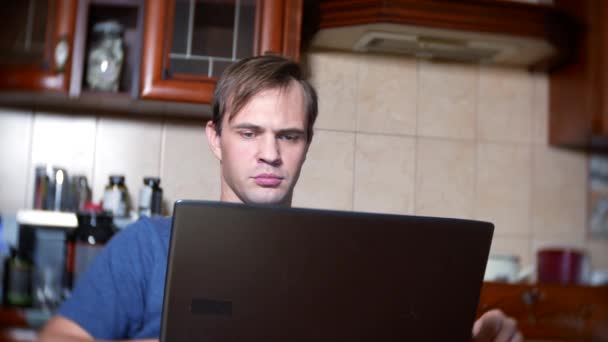 Un hombre sentado en casa en la mesa de la cocina, viendo los cambios en el gráfico de cambio de divisas, mirando el monitor de la computadora. freelancing, 4k, desenfoque de fondo — Vídeo de stock