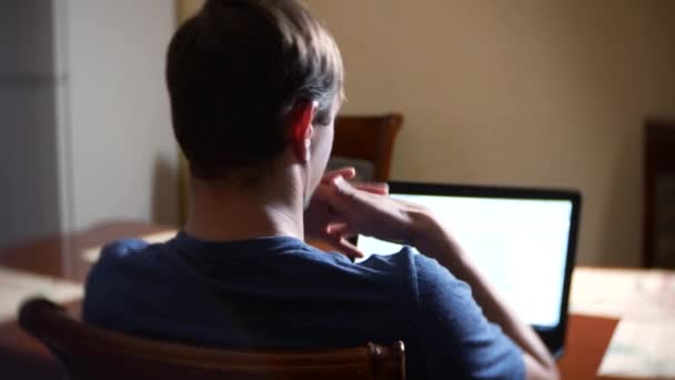 Um homem sentado em casa na mesa da cozinha, observando mudanças no gráfico de câmbio, olhando para o monitor do computador. freelancer, 4k, borrão de fundo — Vídeo de Stock
