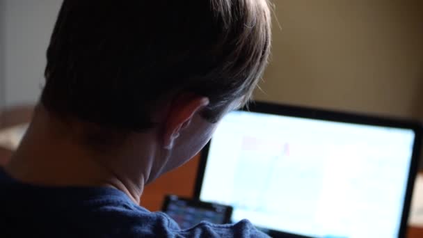 한 남자가 집에서 식탁에 앉아, 통화 교환 차트에 변화를 보고, 컴퓨터 모니터를 보고 있다. 자유롭게, 4 k, 배경 흐림 — 비디오
