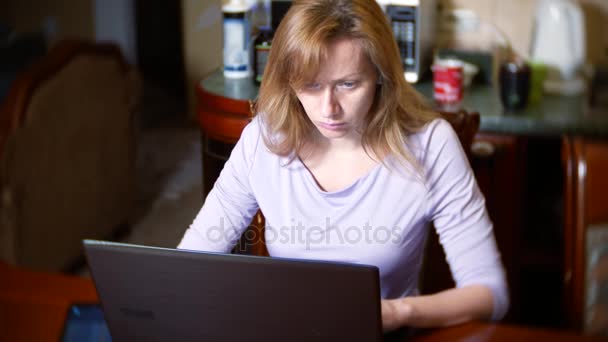 Μια γυναίκα σε ένα μπουρνούζι και με βρεγμένα μαλλιά στο σπίτι κάθεται στον καναπέ, βλέποντας αλλαγές στο γράφημα ανταλλαγής νομίσματος, βλέπουν την οθόνη του υπολογιστή, ελεύθερος επαγγελματίας, 4k, θάμπωμα του φόντου — Αρχείο Βίντεο