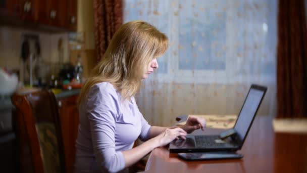 Una mujer en un albornoz y con el pelo mojado sentado en casa en el sofá, viendo los cambios en el gráfico de cambio de divisas, mirando el monitor de la computadora, freelancing, 4k, difuminando el fondo — Vídeo de stock