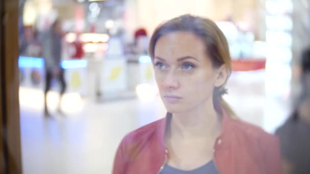 Uma mulher a olhar para uma vitrine na loja. 4k, borrão de fundo . — Vídeo de Stock