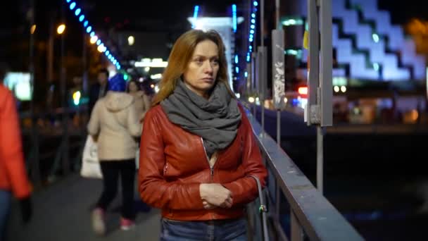 Uma mulher em um cais iluminado da noite, em uma noite fria do outono pelo rio. 4k, borrão de fundo — Vídeo de Stock