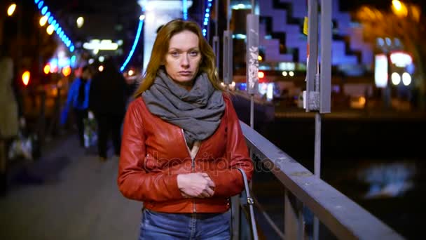 En kvinna på en natt upplyst quay, på en kall höstkväll vid floden. 4k, bakgrundsoskärpa — Stockvideo