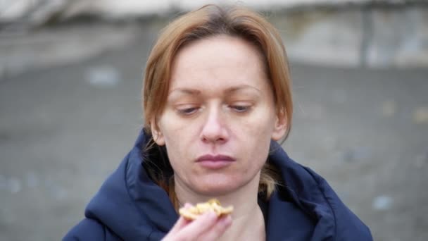 4k. o femeie într-o capotă mănâncă o pizza plimbându-se de-a lungul mării în vreme rece, tulbure . — Videoclip de stoc