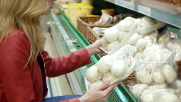 Молодая женщина выбирает еду в продуктовом магазине, женщина делает покупки в супермаркете. 4K, размытие фона — стоковое видео