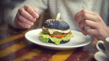 Siyah bir burger bir restoranda yemek bir beyaz kazaklı adam. 4k.