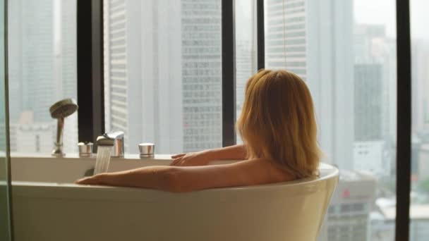 Hermosa mujer disfrutando de un baño relajante en un baño de lujo con ventana. Concepto de estilo de vida y cuidado de belleza. vista desde la ventana a los rascacielos. 4k — Vídeos de Stock