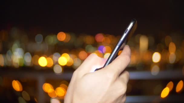 Manos Usando Smartphone al anochecer en la ciudad, Close Up. lectura en el teléfono celular, el uso de las redes sociales de aplicaciones, mensajes de texto. Fondo borroso de luces de la calle nocturna. 4k — Vídeo de stock