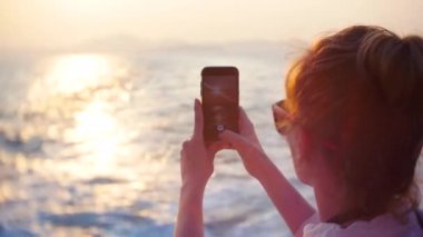 Genç kadın batımında tekne ile seyahat. sosyal ağlar üzerinde yerleştirmek için telefon üzerinde bir fotoğraf yapar. 4k