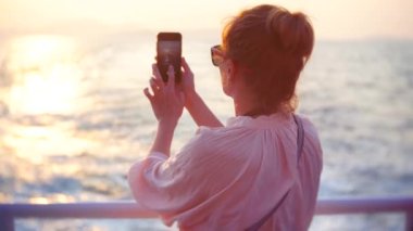 Genç kadın batımında tekne ile seyahat. sosyal ağlar üzerinde yerleştirmek için telefon üzerinde bir fotoğraf yapar. 4k