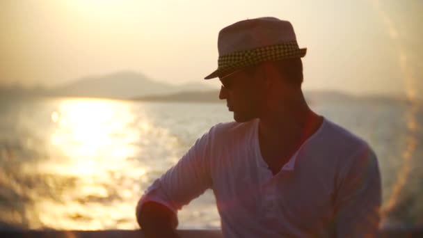 Νεαρός άνδρας στο καπέλο και γυαλιά ηλίου που ταξιδεύουν με σκάφος στο ηλιοβασίλεμα. 4k — Αρχείο Βίντεο