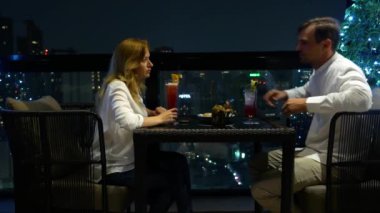 Mutlu bir çift söz ve geceleri, gökdelenler, manzaralı bar terasında kokteyl içme 4k, arka plan bulanıklık