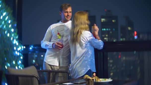 Coppia felice che abbraccia, bacia e beve cocktail sulla terrazza del bar con vista sui grattacieli, di notte, 4k, sfondo sfocato. appuntamento romantico, luna di miele . — Video Stock