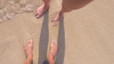 İki sevgili, kumun üzerinde açık güneşli bir günde ayağa. bir erkek ve bir kadın, sahilde bacaklar. 4k, ağır çekim