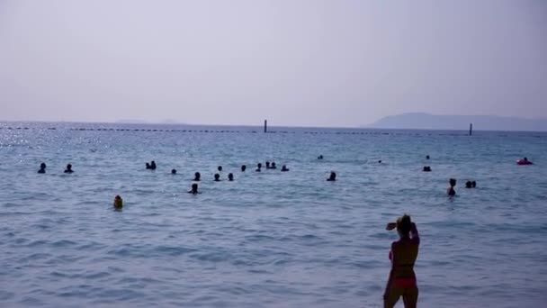 Большая группа неузнаваемых людей в силуэте на пляже и в море. Люди купаются в море. 4k, slow motion — стоковое видео
