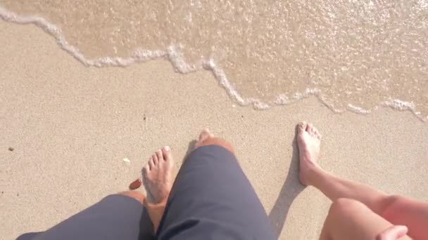 Un par de amantes paseando por la playa en un claro día soleado. piernas de un hombre y una mujer caminando a lo largo de la orilla del mar. 4k, cámara lenta — Vídeo de stock