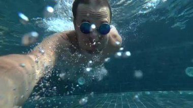 Bir eylem fotoğraf makinesinde bir sualtı selfie yaparken genç beyaz yakışıklı erkek. Kendini kameraya su altında kalktıktan gözlüklü genç bir adam portresi. 4k