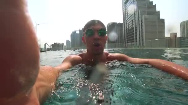 En ung vit stilig hane gör en undervattens selfie på en actionkamera. Porträtt av en ung man med glasögon som lyfter sig själv i kameran under vatten. 4k — Stockvideo