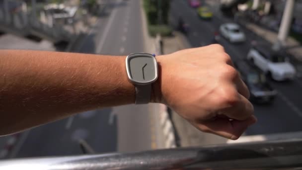 Close-up. horloge op een mans hand, tegen een achtergrond van een stad straat met veel verkeer. Langzame beweging, achtergrond wazig. 4k — Stockvideo