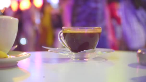 Чашка горячего кофе на столе в кафе, на террасе с видом на оживленную пешеходную улицу. вечерний, подсветка, 4к, размытие фона — стоковое видео