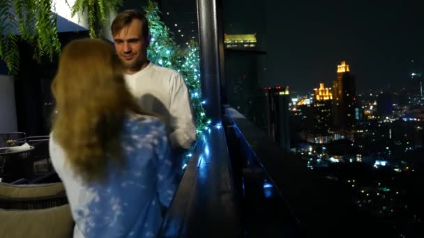 Pareja feliz abrazando, besando y bebiendo cócteles en la terraza del bar con vistas a los rascacielos, por la noche, 4k, fondo borroso. cita romántica, luna de miel . — Vídeos de Stock