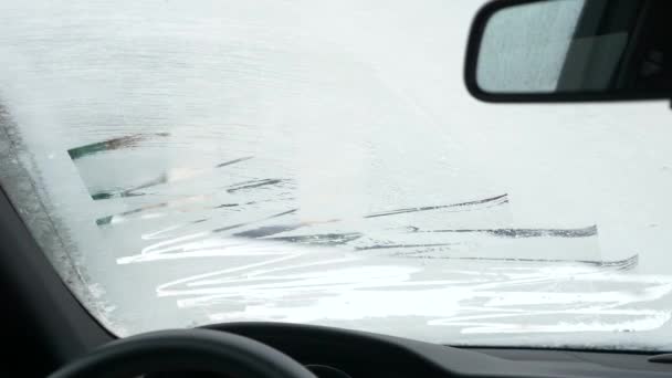 Una mano de mujer con una manicura y un reloj inteligente limpia la nieve de la ventana del coche con un rascador en invierno, una vista desde el interior. 4k — Vídeo de stock