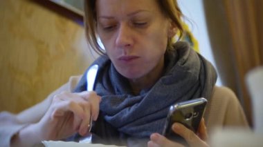 bir kadın bir smartphone kullanarak bir kafede yemek yiyorlar. 4k