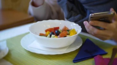 bir kadın bir smartphone kullanarak bir kafede yemek yiyorlar. 4k