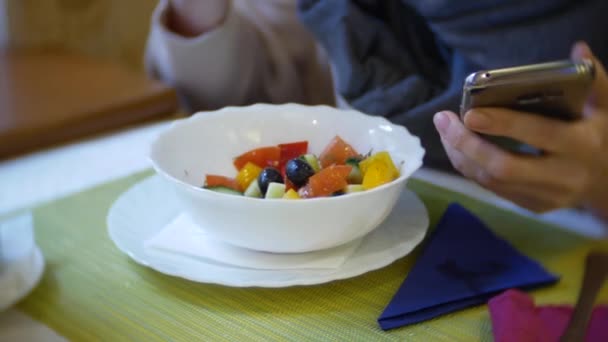 Eine Frau isst mit ihrem Smartphone in einem Café zu Abend. 4k — Stockvideo