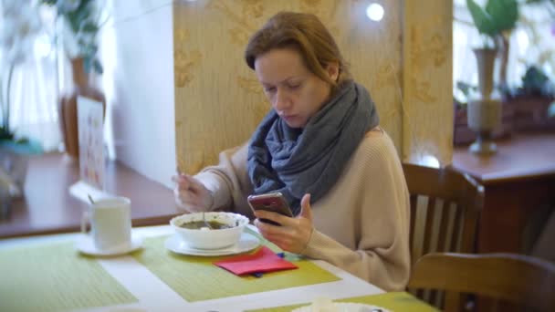 En kvinna är att ha middag på ett café med en smartphone. 4k — Stockvideo