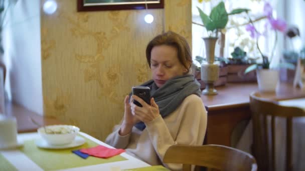 Una mujer está cenando en un café con un teléfono inteligente. 4k — Vídeos de Stock