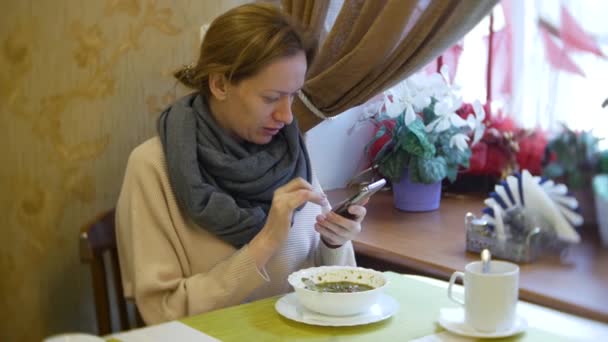 Una mujer está cenando en un café con un teléfono inteligente. 4k — Vídeos de Stock